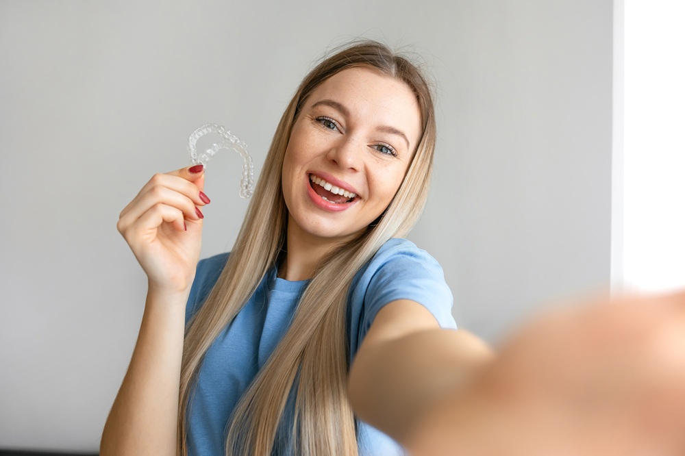 A cheerful woman proudly holds her Invisalign aligner, enjoying the confidence of a straighter smile achieved through clear and removable aligners. – Invisalign