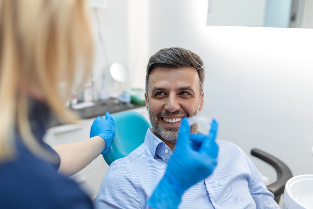 A dentist presents an Invisalign aligner to a smiling patient, explaining the steps of achieving a perfectly aligned smile with modern orthodontic care. – Invisalign