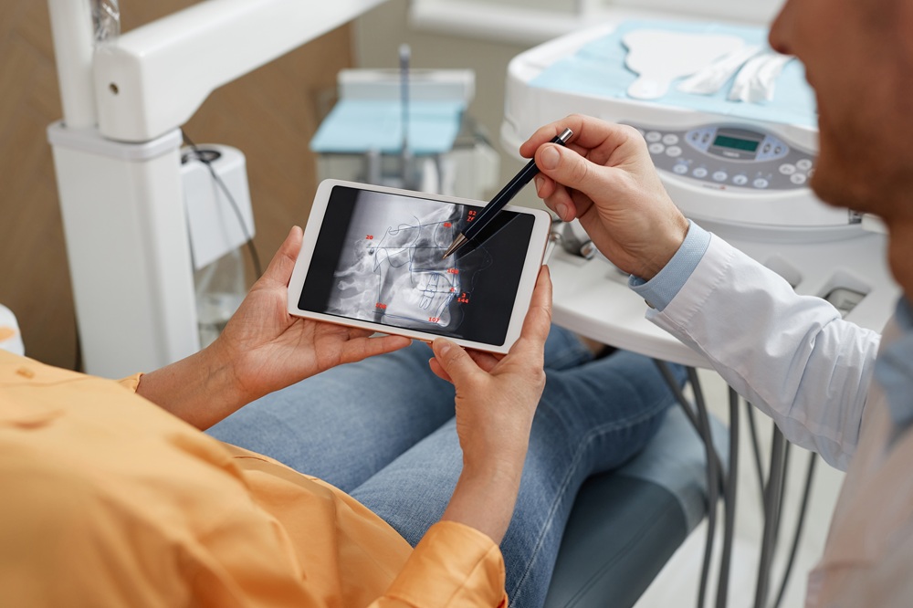 Dentist Reviewing 3D Dental Scan – Cone Beam CT Scan A dentist analyzes a 3D dental scan on a tablet to assess bone structure and treatment options, demonstrating advanced imaging capabilities in modern dentistry. – Cone Beam CT Scan