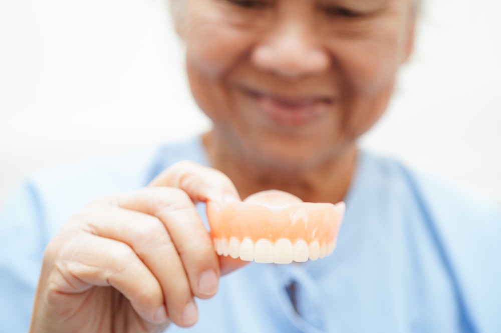 A patient carefully holds a set of complete dentures, representing restored function and confidence through modern dental solutions. – Dentures in Seattle