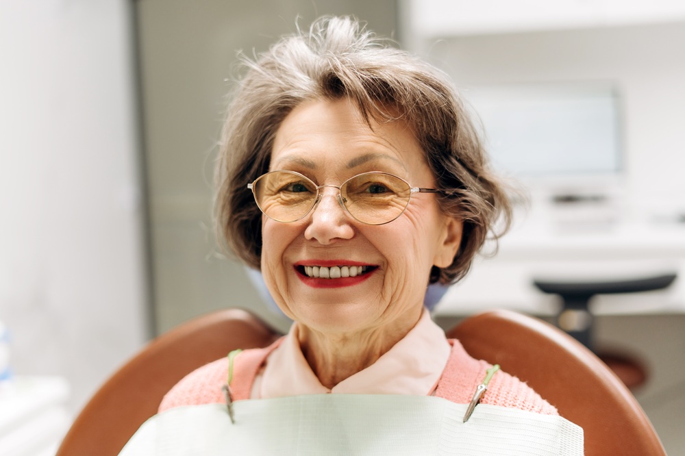 A senior woman smiles proudly in the dental chair after receiving well-fitted dentures that restore her natural smile and comfort. – Dentures in Seattle