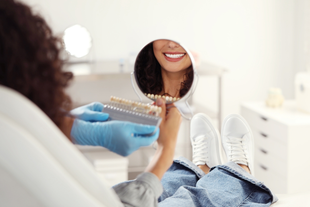 A patient holds a mirror while the dentist checks tooth shade, ensuring a restored, natural-looking smile after emergency dental care. – Emergency Dentist Seattle