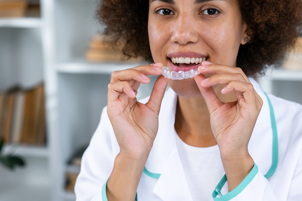 A smiling dental professional demonstrates a clear aligner used in Invisalign treatment, showcasing a comfortable and discreet way to straighten teeth. – Invisalign