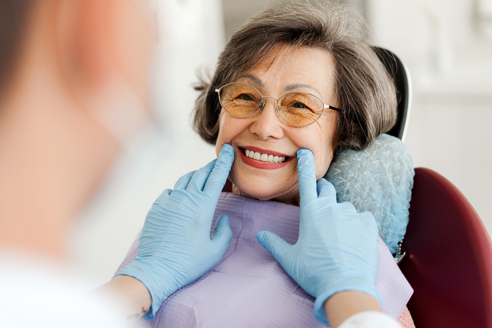 Senior Patient Smiling After Dental Evaluation – Digital X-Ray A cheerful senior woman smiles in the dental chair as her dentist reviews digital X-rays to ensure the health and alignment of her teeth. – Digital X-Ray