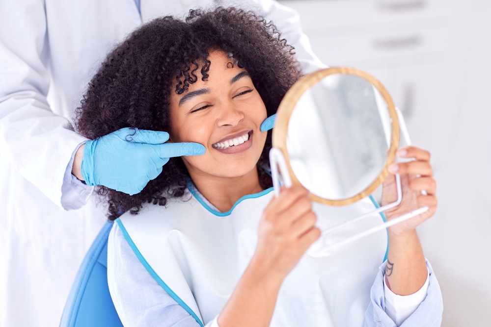 Patient Smiling After Root Canal Treatment – Root Canals A happy patient checks her restored smile in the mirror after a successful root canal procedure that relieved pain and preserved her natural tooth. – Root Canals