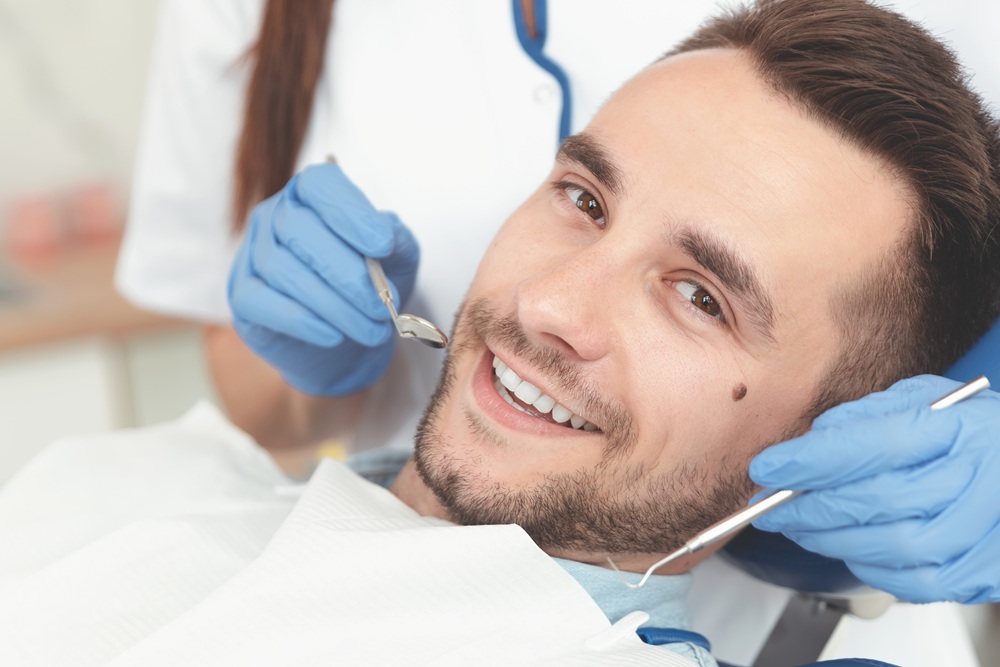 Smiling Patient During Dental Visit – General Dentistry A cheerful patient relaxes in the dental chair while receiving a professional examination and cleaning to maintain a healthy smile. – General Dentistry