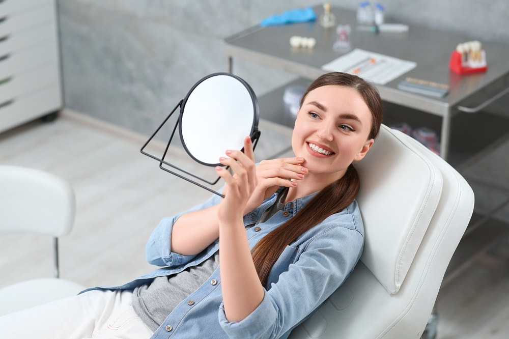 A woman smiles while checking her reflection after receiving dental implants, pleased with her restored confidence and beautifully renewed smile. – Dental Implants