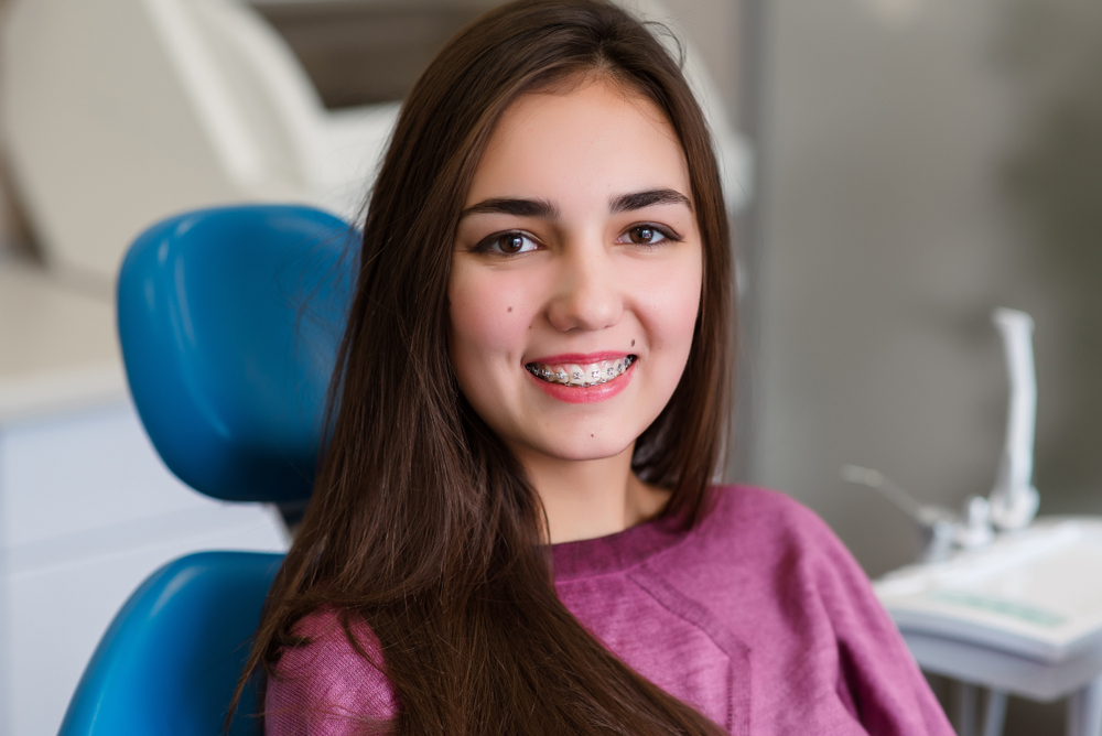 A young dental patient smiles confidently in the chair, showing healthy teeth and braces after a successful emergency dental visit. – Emergency Dentist Seattle