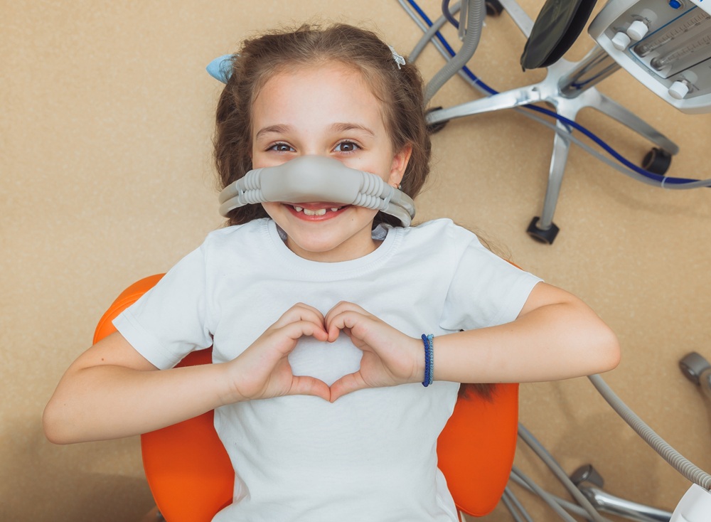 A happy young patient gives a heart sign while receiving safe, gentle sedation to ease anxiety and ensure a comfortable dental visit. – Sedation Dentistry