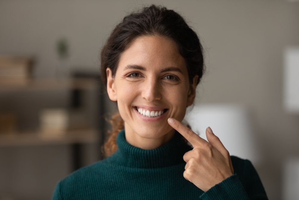 A woman proudly points to her bright smile, representing the relief and renewed confidence that comes after effective emergency dental treatment. – Emergency Dentist Seattle
